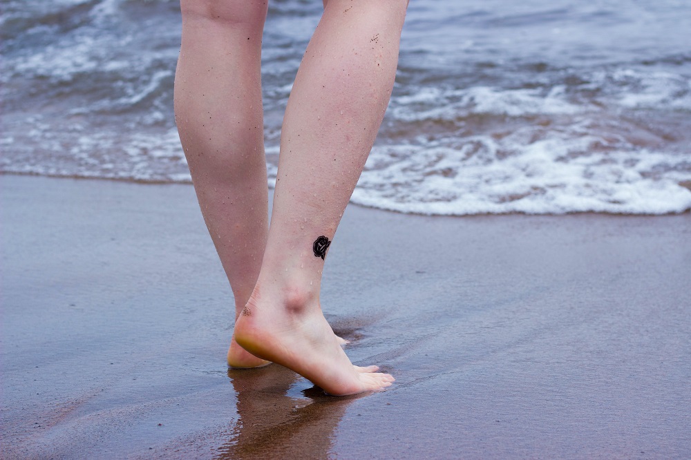 Woman standing barefoot on the sand beach by the ocean