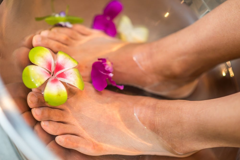 Woman soaking feet on water with exotic flowers