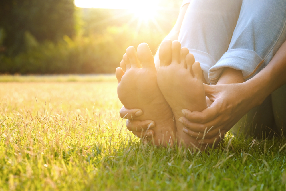 Foot Pain Leg of man sitting on grass in the park holding he feet and stretch the muscles in morning sunlight